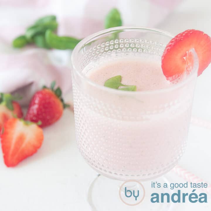 een vierkante foto met een glas met aardbeiensmoothie. Gegarneerd met aardbeien en basilicum