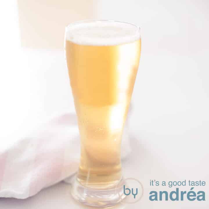 Een vierkante foto met een bier cocktail van pils en appelcider op een witte ondergrond. Een roze witte theedoek erachter.