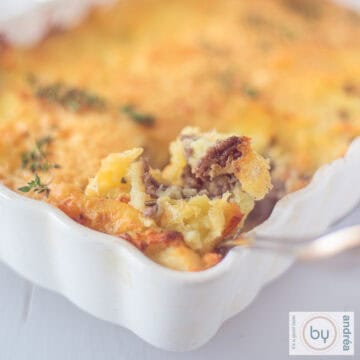 Een vierkante foto van een deel van een ovenschotel met aardappelpuree en rundergehakt. Een lepel nam een ​​schep.
