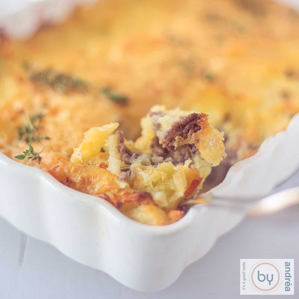 Een vierkante foto van een deel van een ovenschotel met aardappelpuree en rundergehakt. Een lepel nam een   schep.