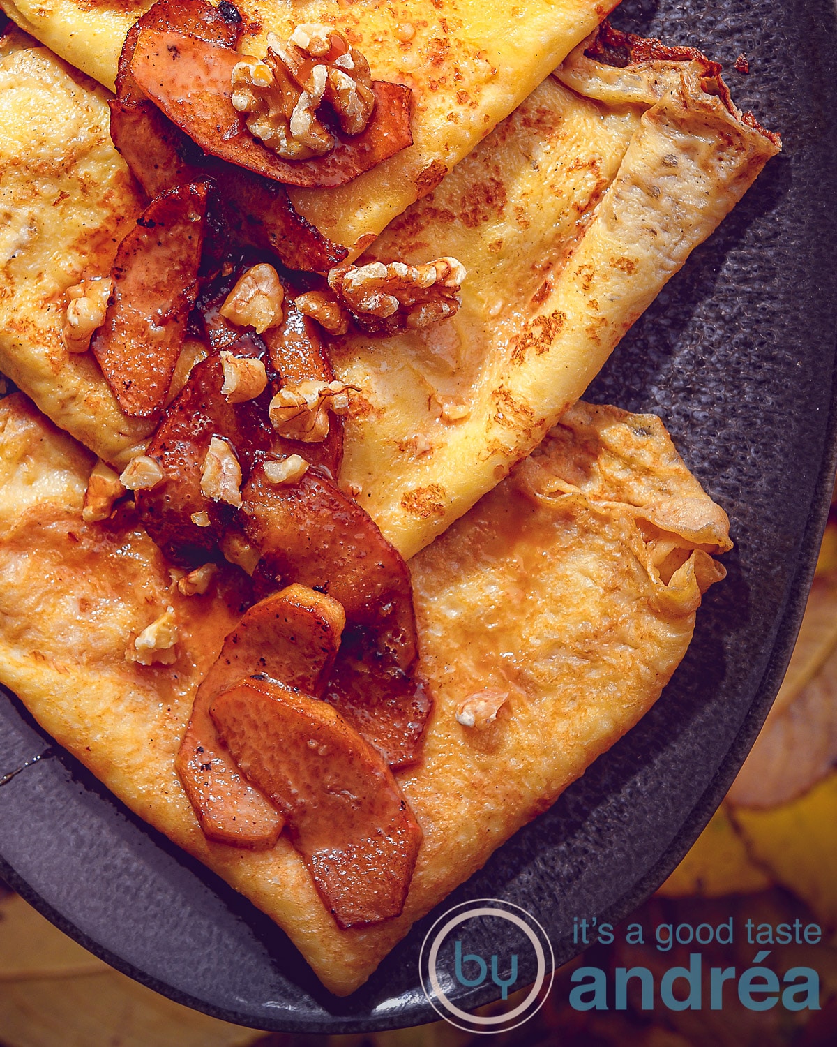 Een hoogtefoto met een grijze schaal op een blad achtergrond met een macro vergroting van crepes met karamelsaus en gebakken appeltjes