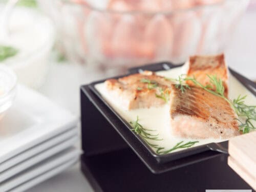 Een vierkante foto met een gourmetschaaltje gevuld met drie blokjes gemarineerde zalm in een dille roomsaus