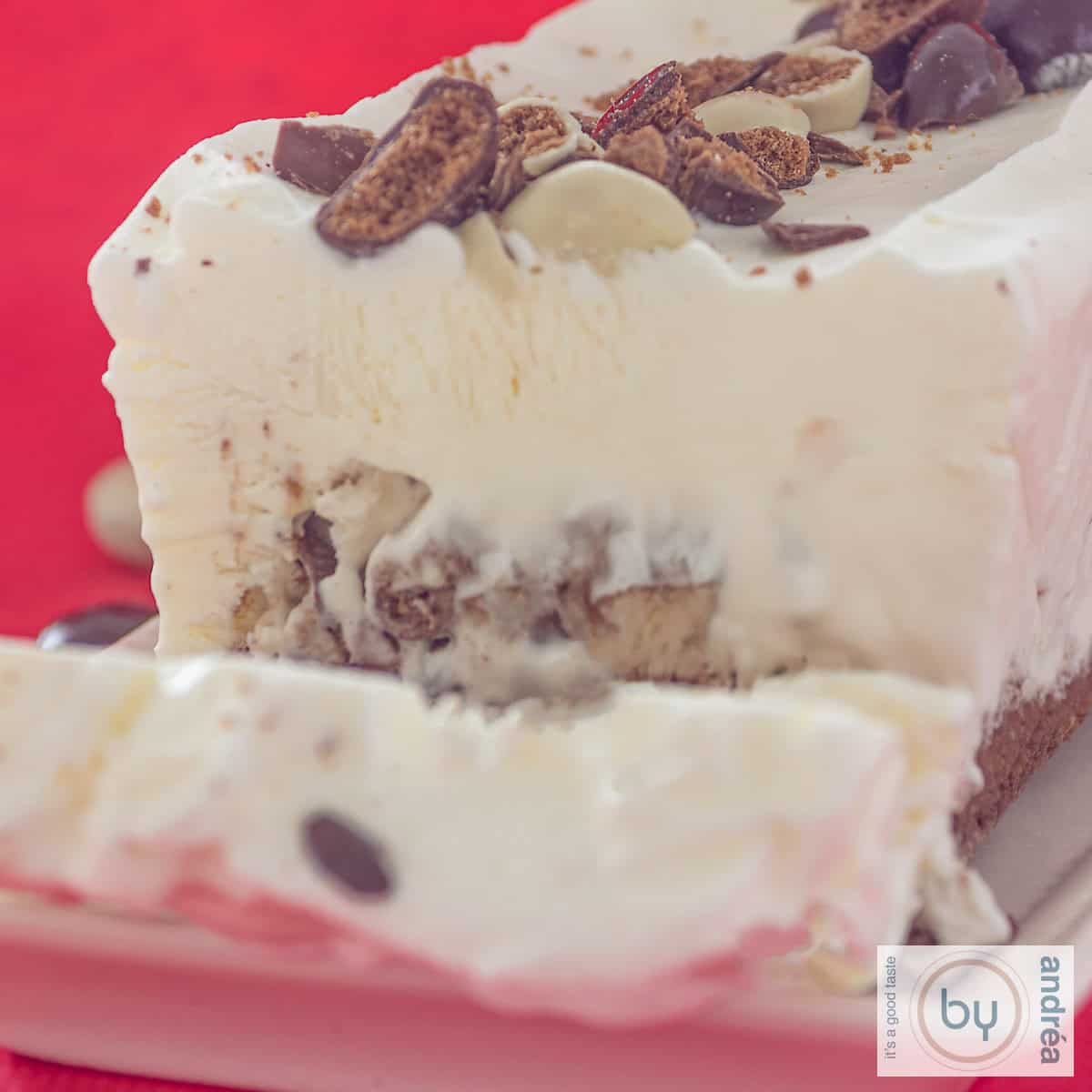 Een vierkante foto van een ijstaart met chocolade kruidnoten. Een plakje erafgesneden.