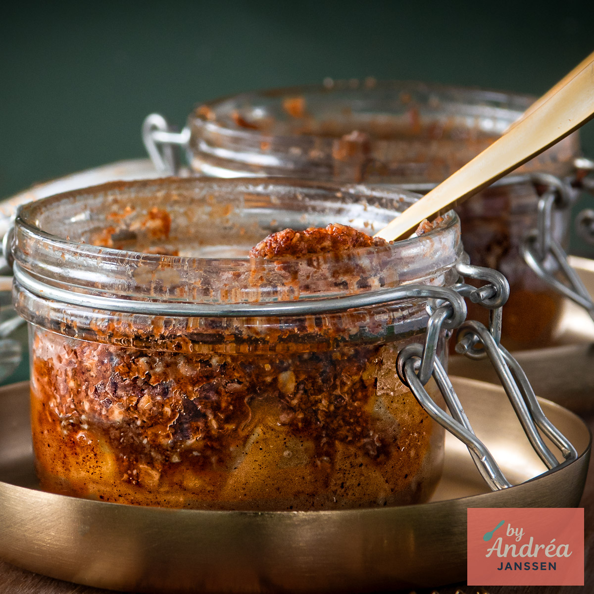 Close-up van appelstukjes onder een gebakken havermoutkruimellaag in een weckpotje, met een tweede potje op de achtergrond.