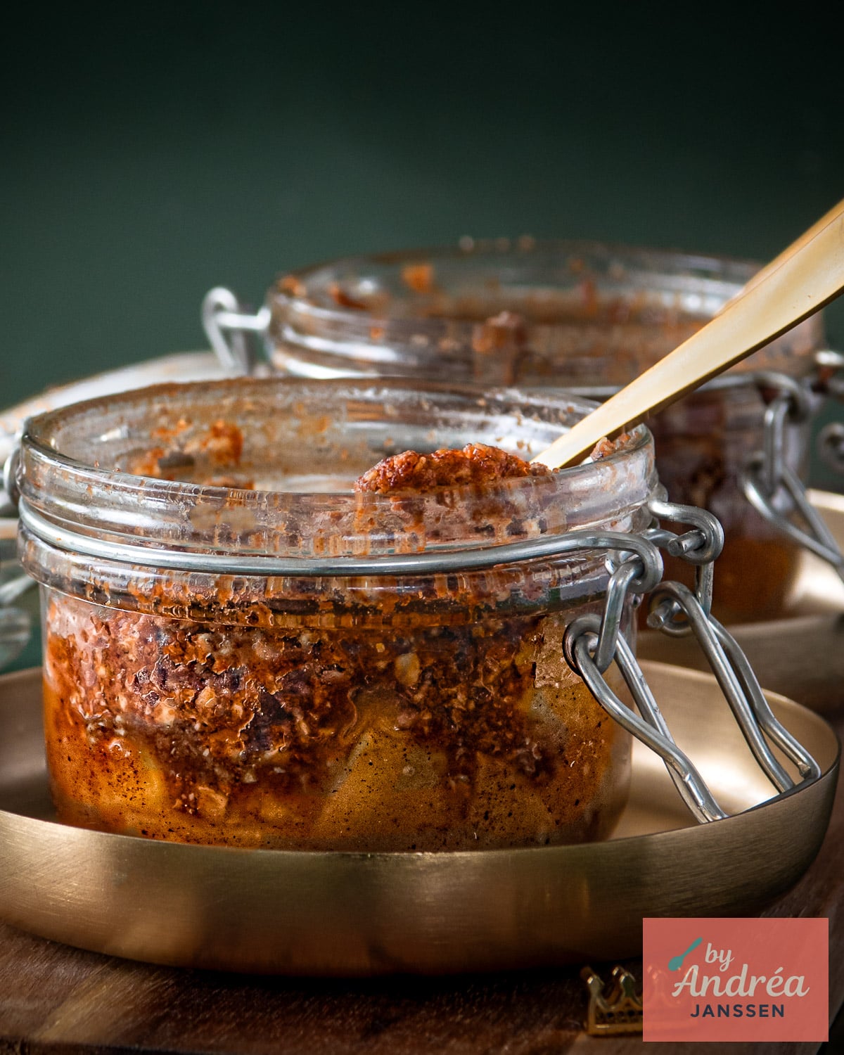 Appelkruimeltaart met een bruin gebakken havermoutlaag in een weckpotje met een goudkleurige lepel op een dienblad.