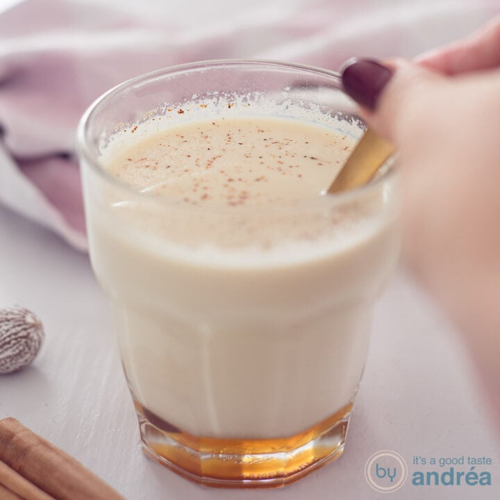 Een vierkante foto met in het midden een glas gevuld met chai thee met melk en honing. Een gouden lepel roert in het glas.