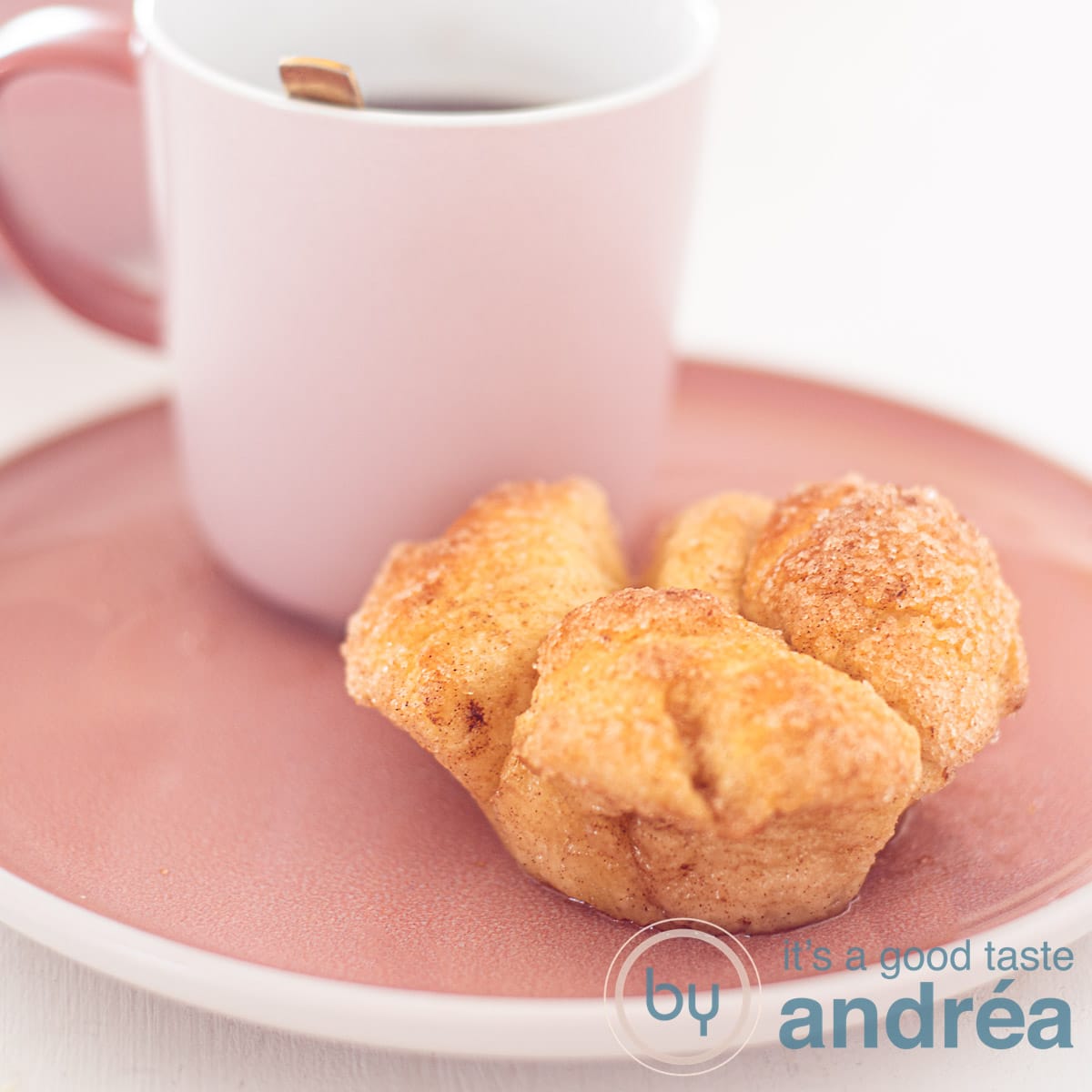 Een vierkante foto van een roze bord met daarop een kopje koffie en daarvoor een monkey bread muffin.
