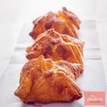 Een vierkante foto met drie appel pakketjes met bladerdeeg gebakken in de oven.