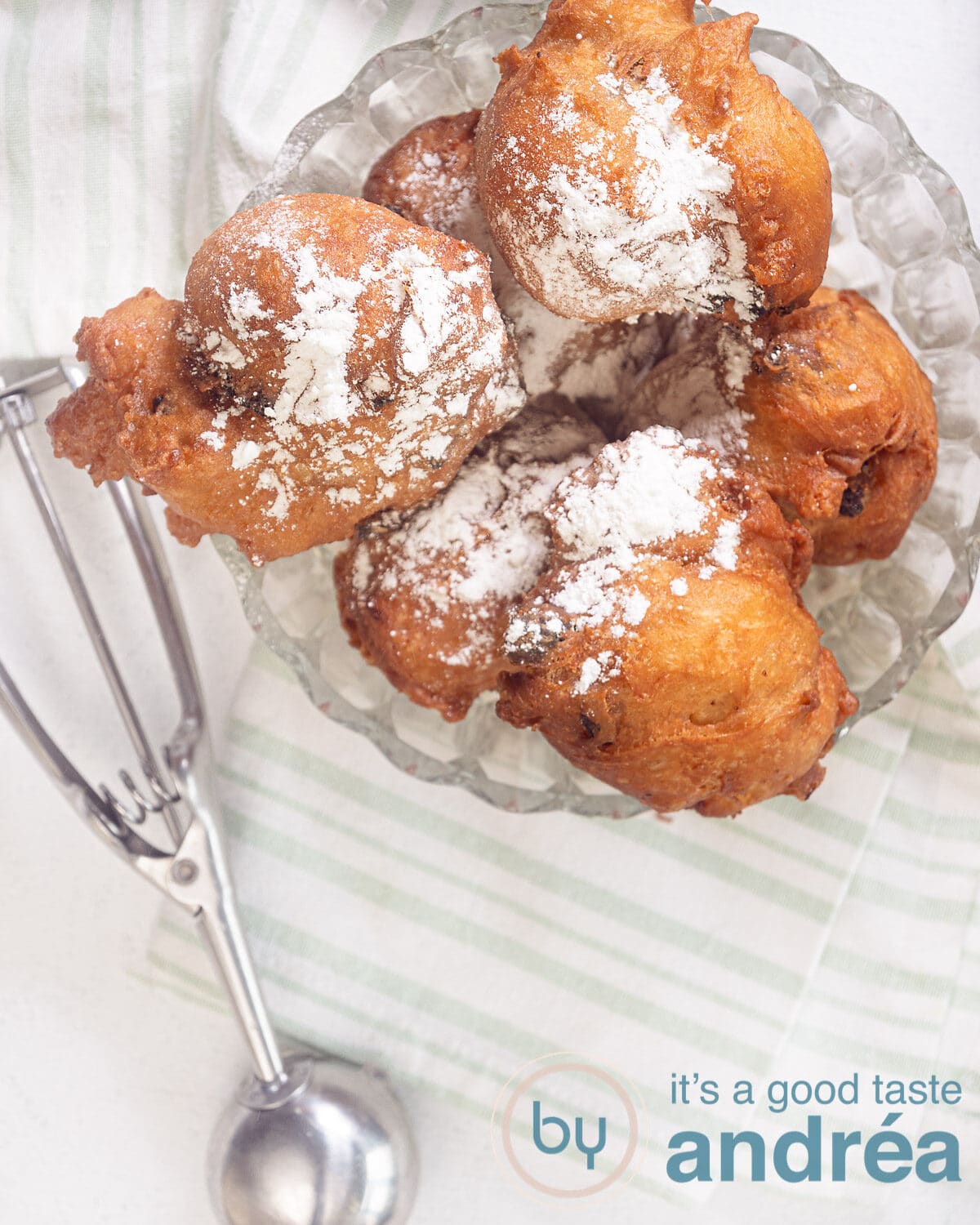 een topfoto van een glazen schaal gevuld met oliebollen. Onderin een ijsschep