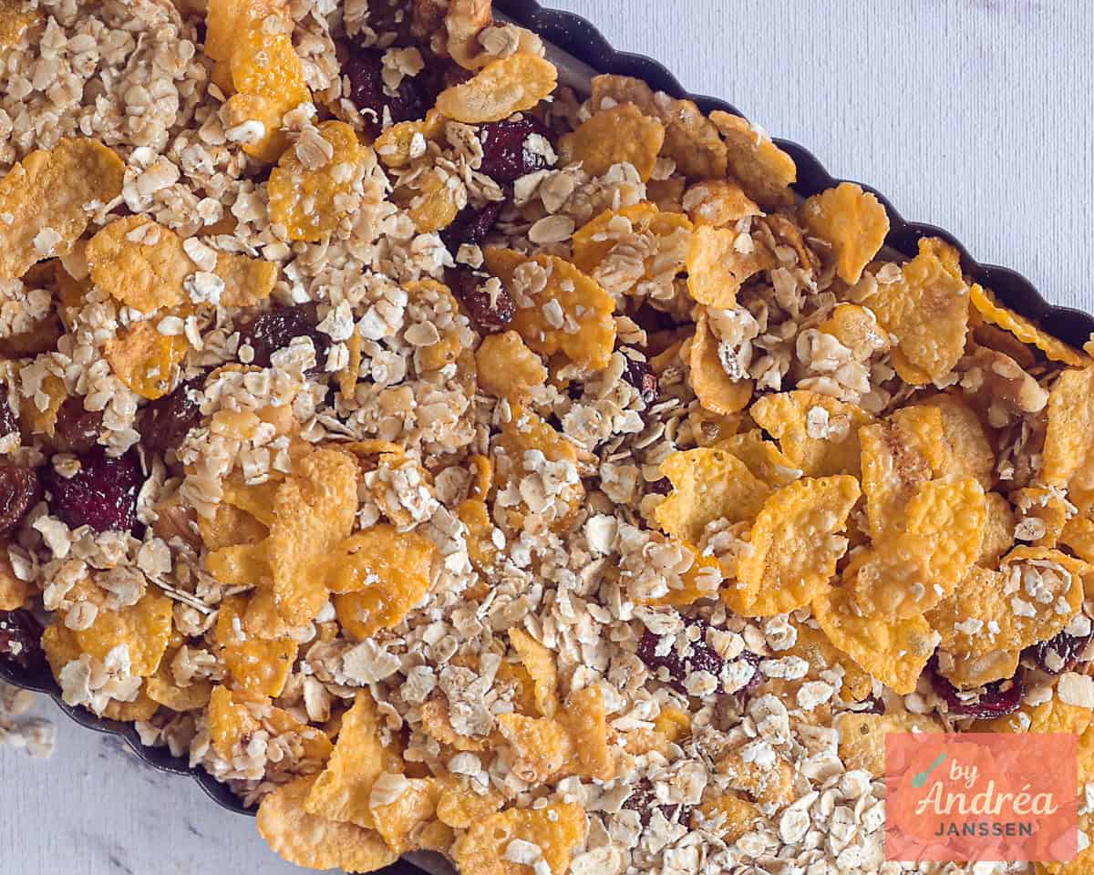 Het mengsel van cornflakes en havermout met fruit en noten wordt in een bakvorm gedaan.