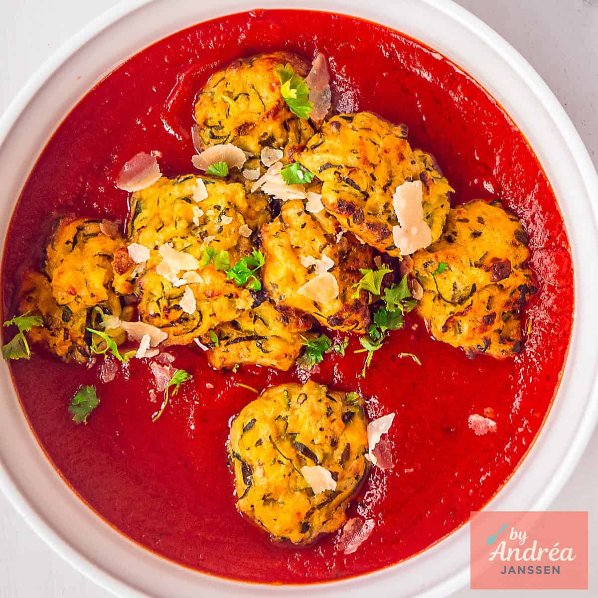 Een vierkante foto van een witte schaal met tomatensaus en gehaktballetjes van courgette, lekker vegetarisch.