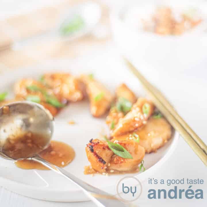 Een vierkante foto met een wit bord met plakjes kip met een honing, knoflook sesam saus gegarneerd met lente ui. een sauslepel met extra saus ligt op het bord