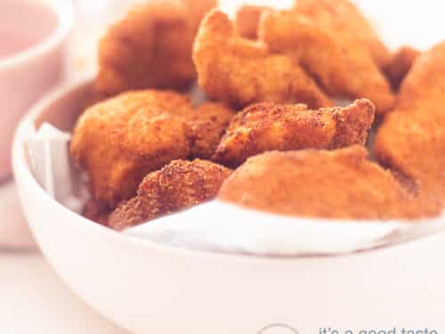 Een vierkante foto met een roze schaal gevuld met kipnuggets. Een witte achtergrond.