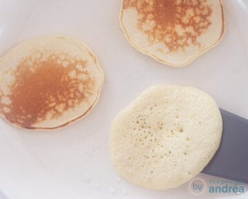 Een witte koekenpan met drie pancakes. Twee al omgedraaid, een wordt net omgedraaid