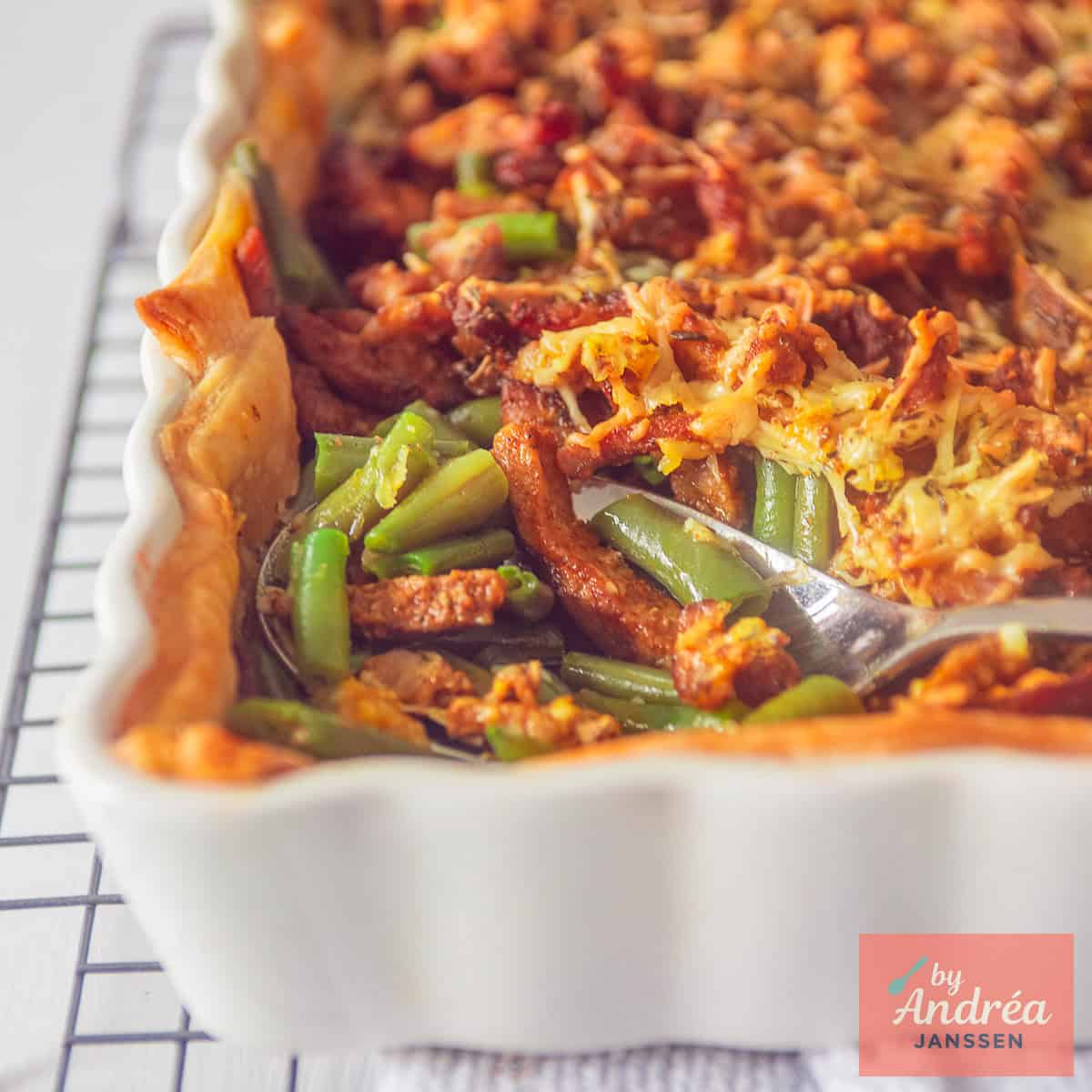 Een vierkante foto met een deel van een witte ovenschaal met bladerdeeg, boontjes, kaas en shoarma vlees.