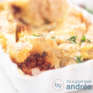 Een vierkante foto met een deel van een witte ovenschaal gevuld met spinazie, gehakt en aardappelpuree.