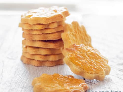 A square picture with a row of cookies on a white wooden plate. Some cookies are hanging against the staple. a sable cookie in front.