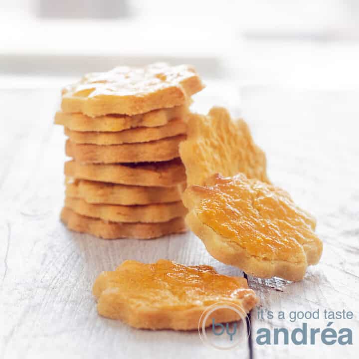 A square picture with a row of cookies on a white wooden plate. Some cookies are hanging against the staple. a sable cookie in front.