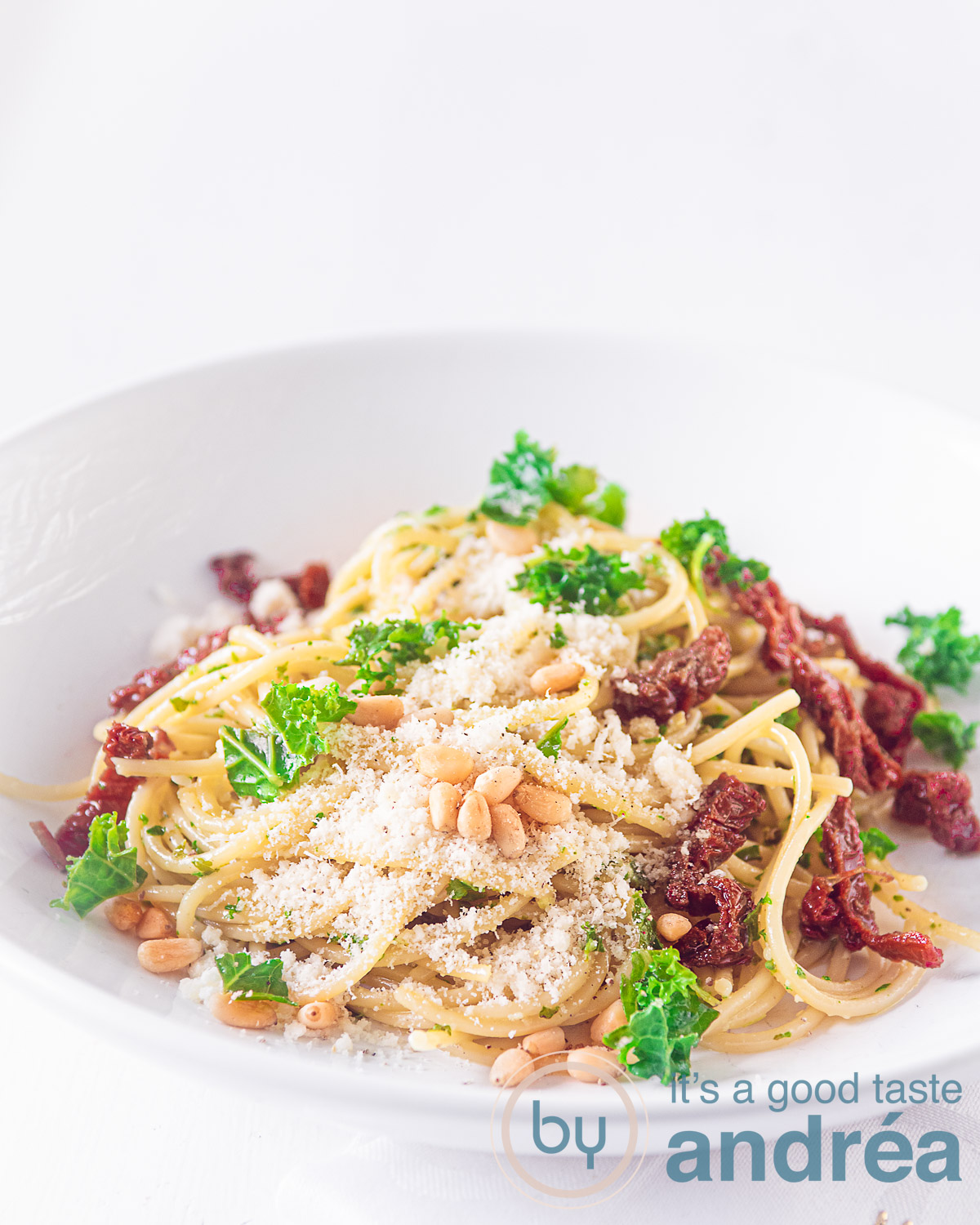 Kale pesto with spaghetti on a white plate garnished with sundried tomatoes, parsley and grated cheese.