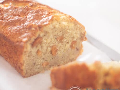 Een vierkante foto van een deel van een bananenbrood gevuld met cashews op een bakpapier.