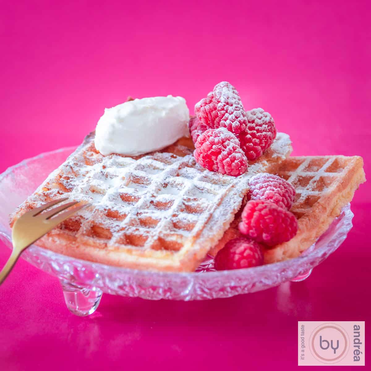 Een vierkante foto met een glazen schaaltje met 2 wafels, frambozen en mascarpone. Een roze achtergrond.