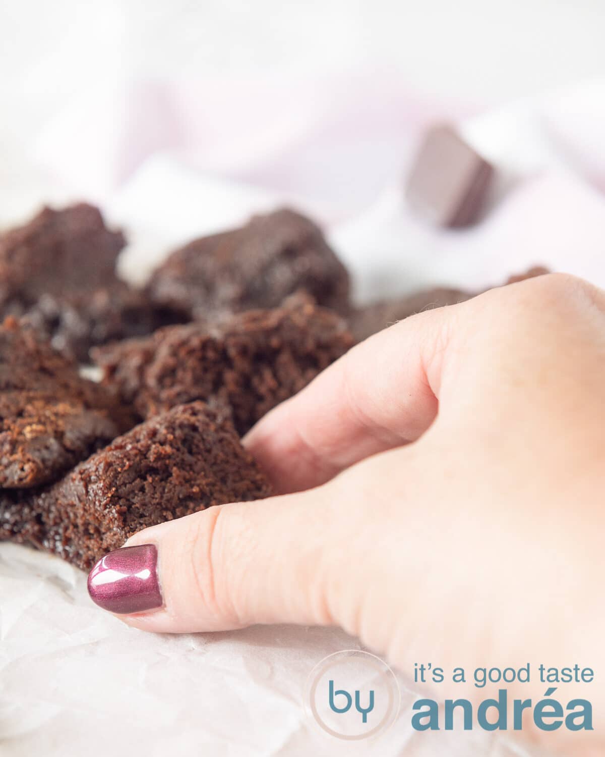 A hand picking a square of brownie on a white underground. A pink and white cloth in the background