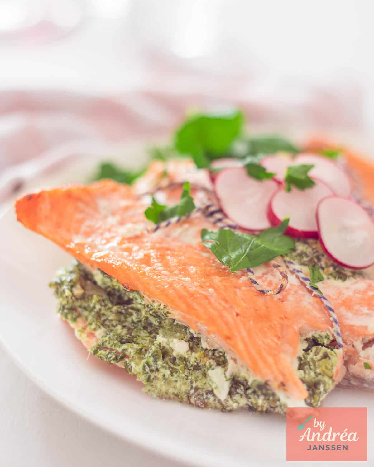 A portion of a stuffed salmon fillet with spinach and celery on a white plate.