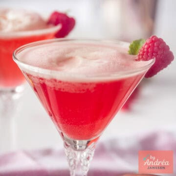 Een vierkante foto met een cocktailglas gevuld met frambozen, gin en Prosecco