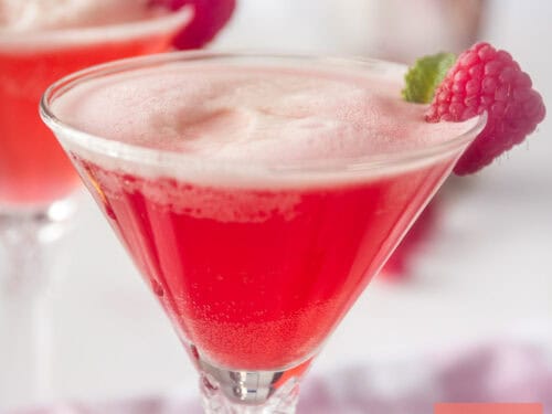Een vierkante foto met een cocktailglas gevuld met frambozen, gin en Prosecco