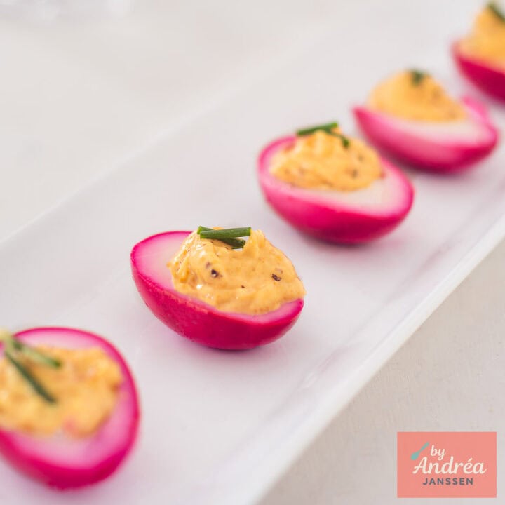 Purple deviled eggs in a row on a white plate