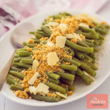 Een vierkante foto met een witte schaal met sperziebonen, Parmezaanse kaas en kruidenpaneer