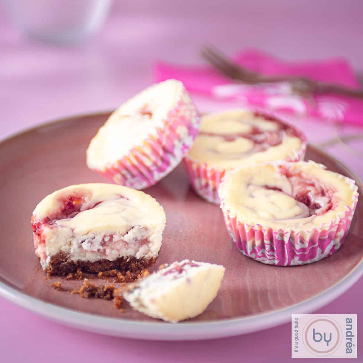 Een vierkante foto met een roze bord met roze cupcakes, vier waarvan 1 doormidden is gebroken en je de bodem goed ziet.