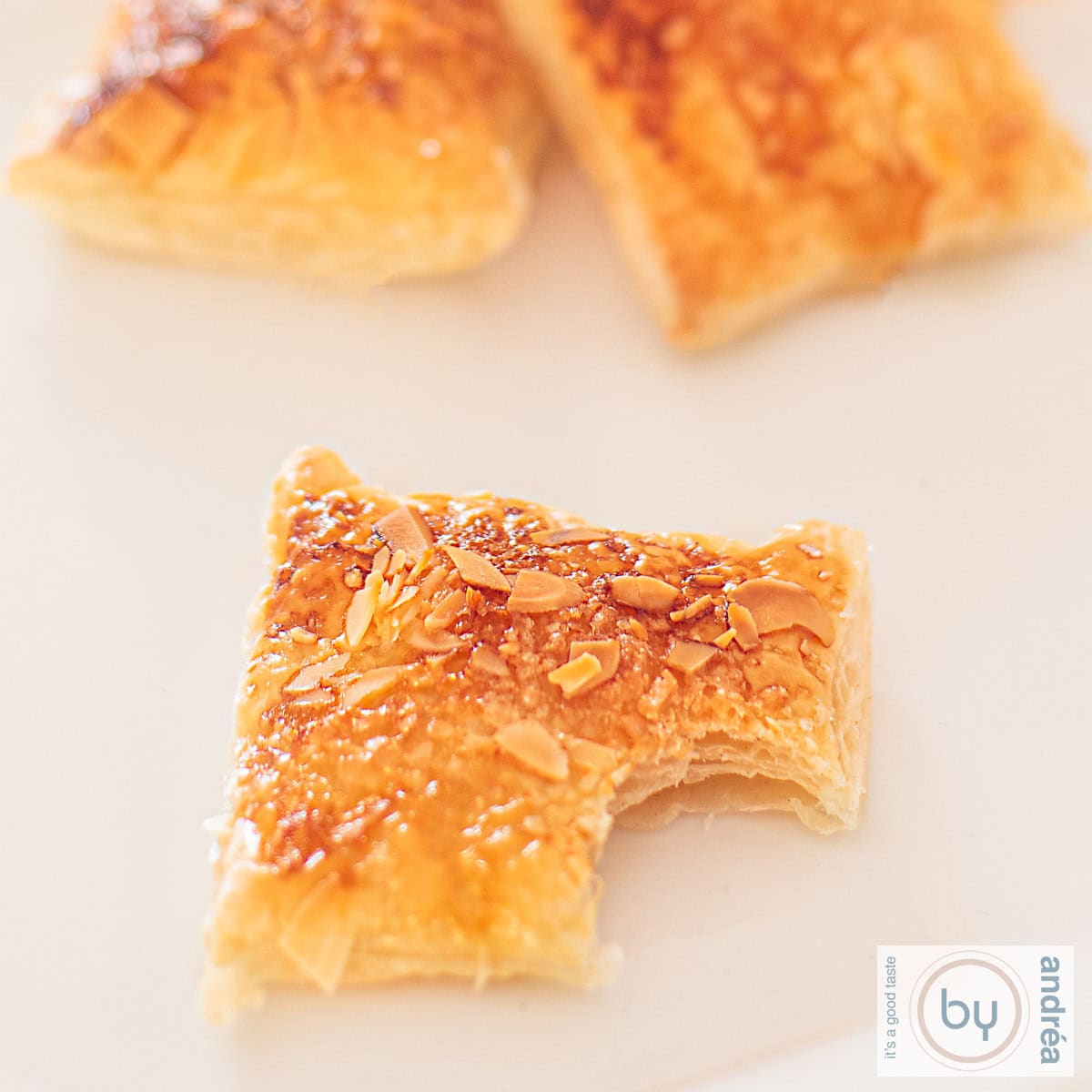 Een vierkante foto met citroenkoekjes met een amandel laag. Een hap is uit het voorste koekje genomen.