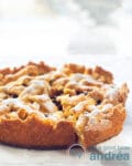 Een foto van een appeltaart op een tafel waar met een taartschep een stuk uit wordt gepakt