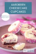 Een roze bord met een roze achtergrond met marmer cheesecake cupcakes, vier stuks. Een tekst bovenin: makkelijk recept, aardbeien cheesecake cupcakes