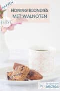 Een wit schaaltje met blondies en een roze witte mok. Een tekst bovenin: honing blondies met walnoten, bakken, makkelijk recept