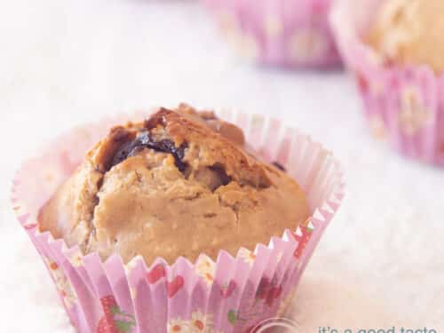 Een vierkante foto met in de voorgrond een muffin met chocola en kokos, glutenvrij en in de achtergrond op een rijtje drie muffins (deels te zien). De muffins staan in geraspte kokos.