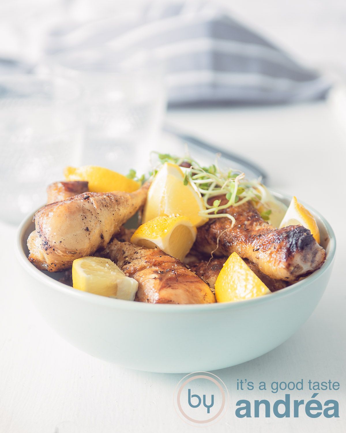 Drumsticks with lemon and cres in a blue bowl on a white background. In the back a grey white cloth