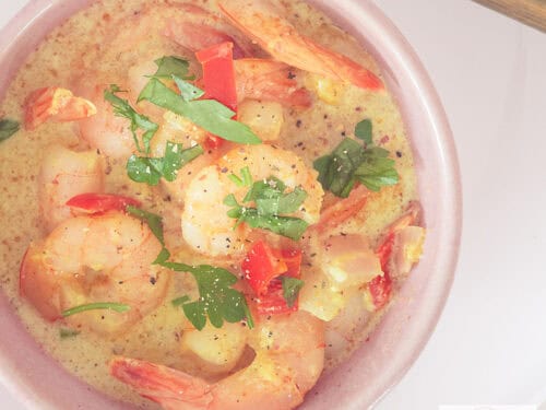Een vierkante foto met een roze kom van bovenaf gefotografeerd gevuld met garnalencurry in kokosmelk.