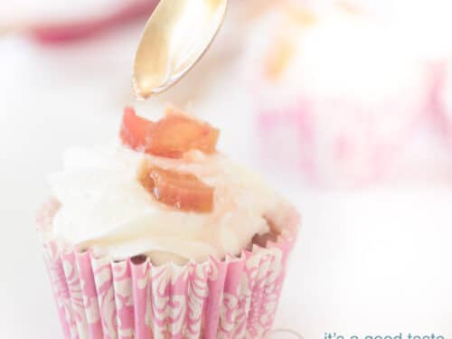 Een vierkante foto van een licht roze cupcake vorm met een slagroom rabarber topping. Van een lepel sprenkelt wat siroop.
