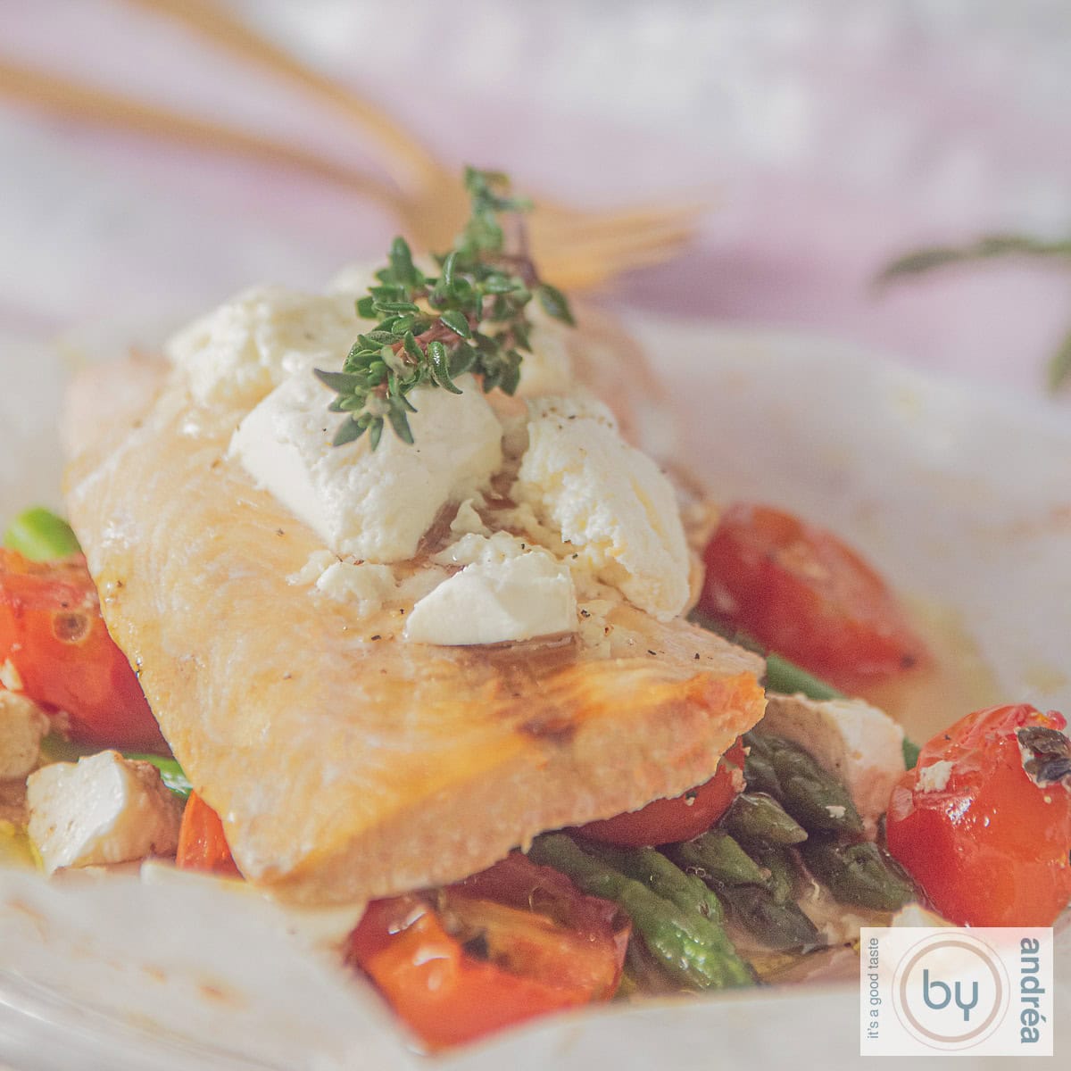 Een vierkante foto met een moot zalm op een bedje van asperges, tomaat en een topping van feta
