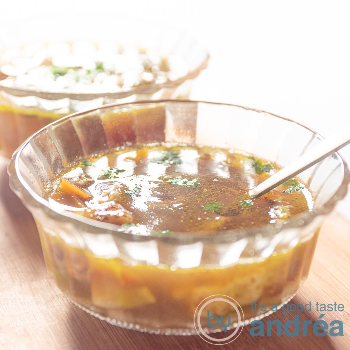 Twee glazen schaaltjes achter elkaar op een houten plank gevuld met groentebouillon met reepjes pannenkoek