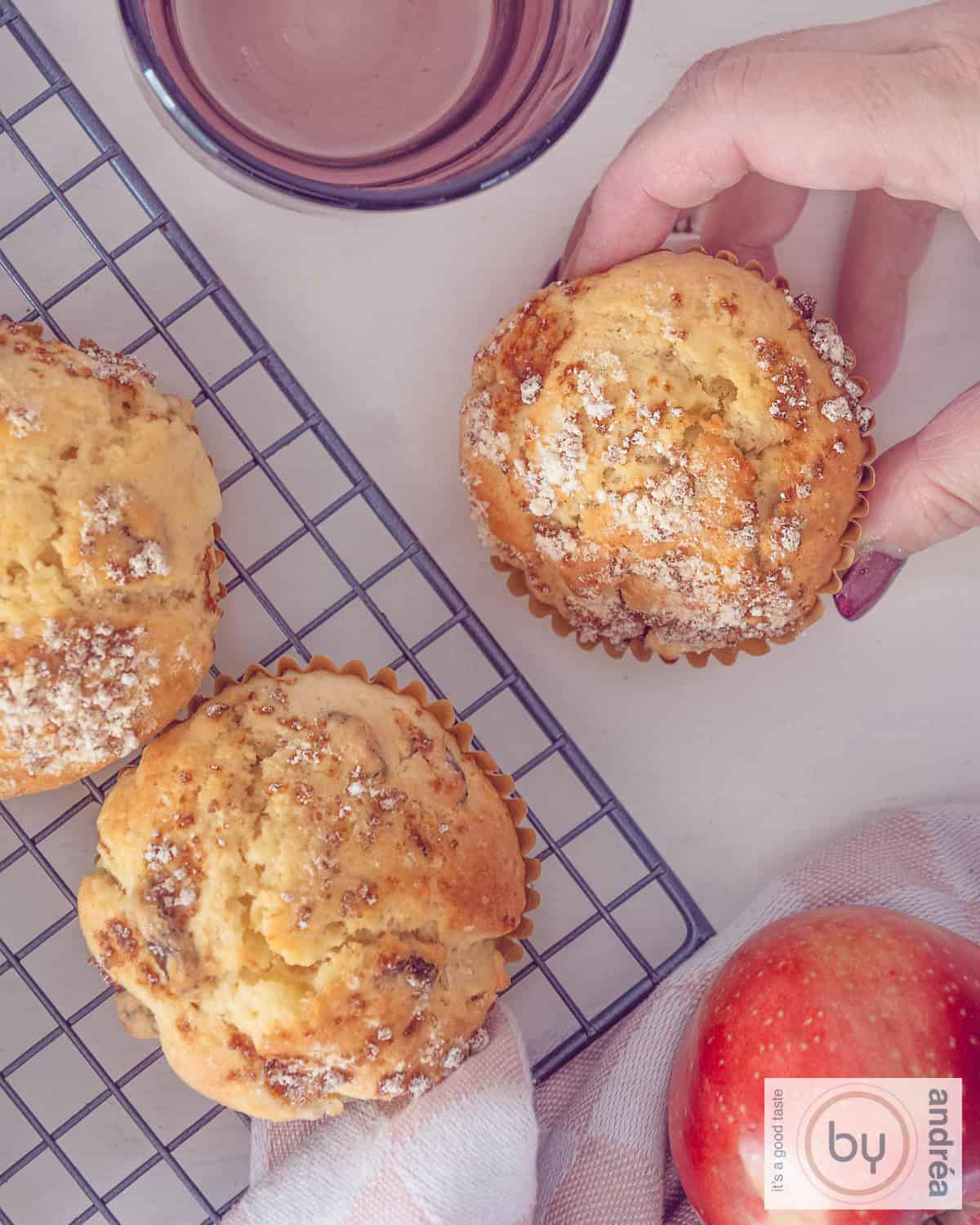A height picture of three raisin apple muffins. A hand takes one of them.