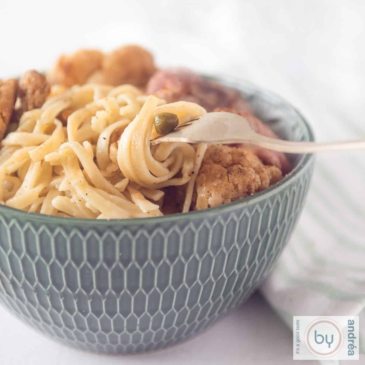 Een vierkante foto van een groene kom gevuld met bloemkool, erwtjes, biefstuk en bami. Een vork met wat bami eromheen gedraaid