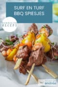 Een witte doek met vijf spiesjes met biefstuk, garnalen en citroen. Een tekst: makkelijk recept, surf en turf BBQ spiesjes