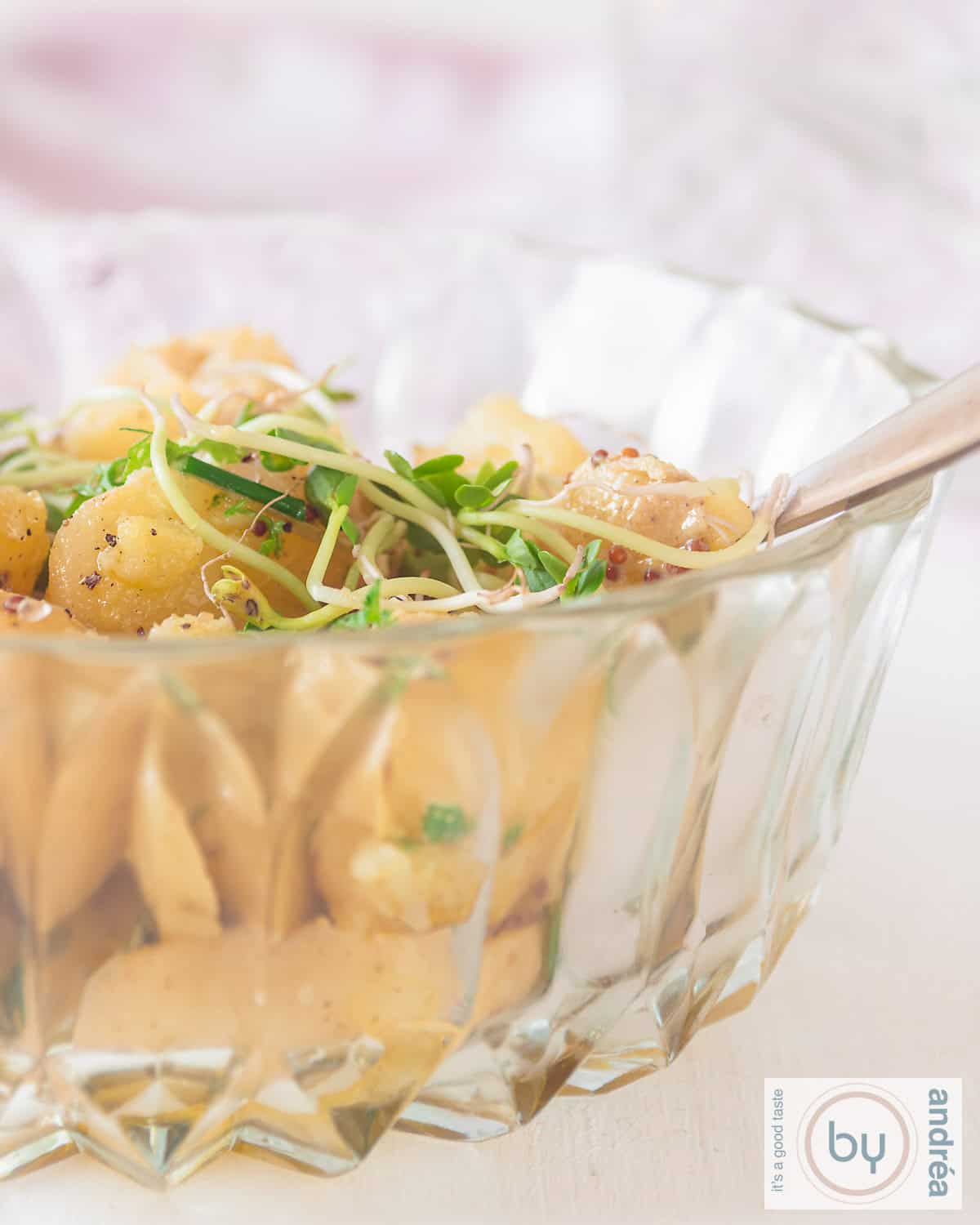 Een glazen schaal gevuld met krieltjessalade met groene kruiden en een mosterddressing.