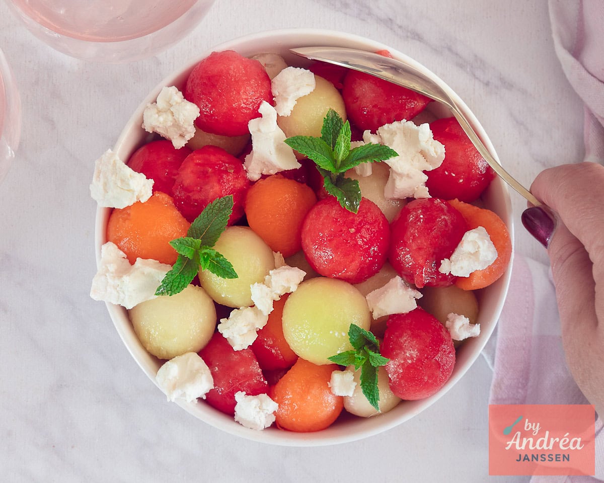 A white bowl with three colored balls of melon, goat cheese and mint