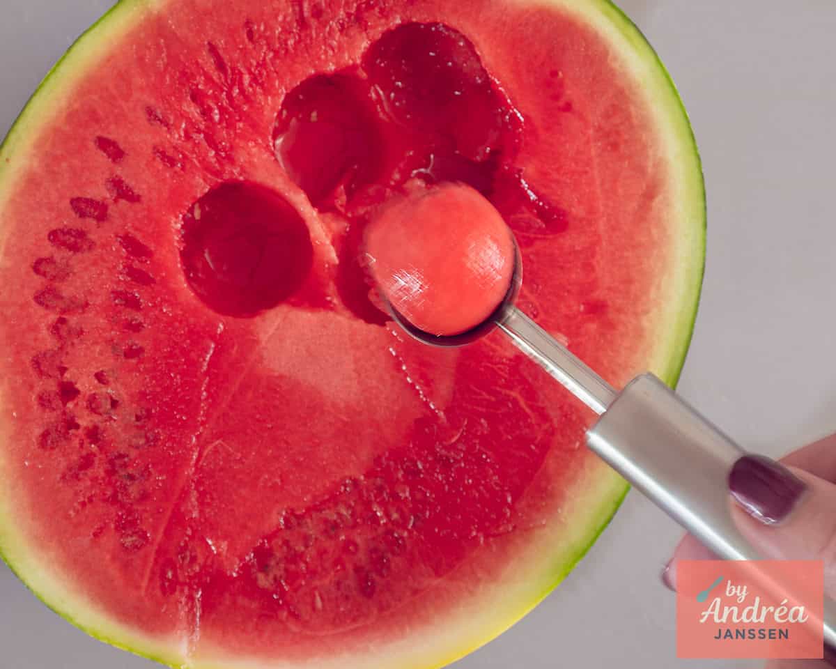 A melon baller over a watermelon holding a ball.