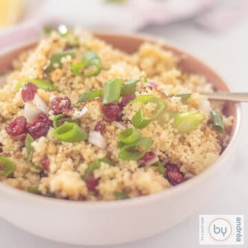 Een vierkante foto met een schaal met couscous met pijnboompitten, citroen en cranberry's