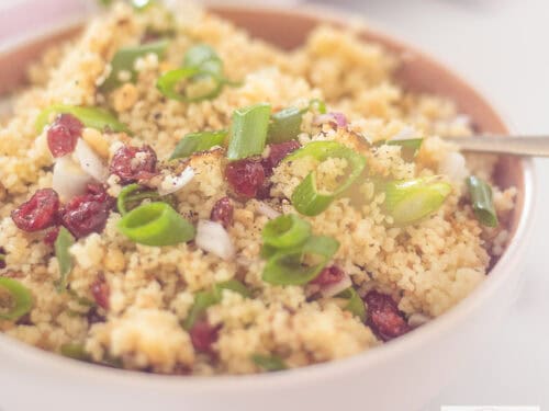 Een vierkante foto met een schaal met couscous met pijnboompitten, citroen en cranberry's